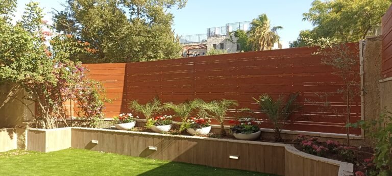 גדר עץ אופקית עם ערוגות מעץ ותאורה בגינה עם מדשאה