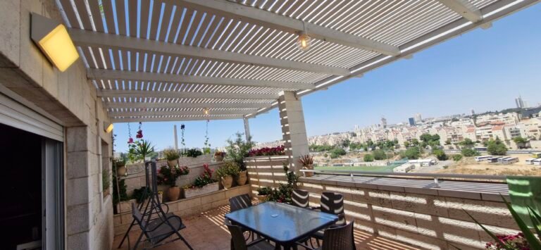 פרגולה לבנה עם שלבי הצללה מעל מרפסת עם פינת אוכל ונוף לעיר