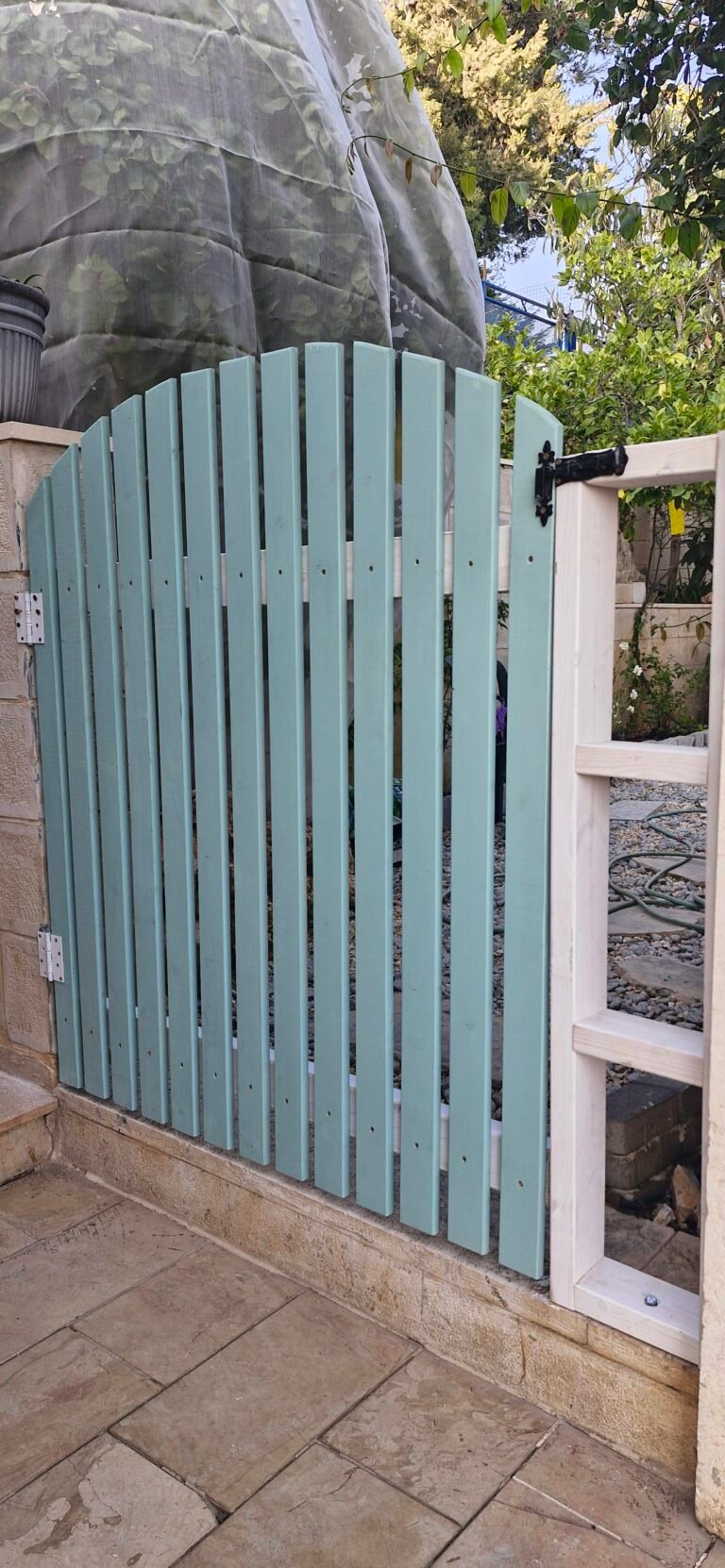 שער עץ מקושת בגוון תכלת בכניסה לחצר