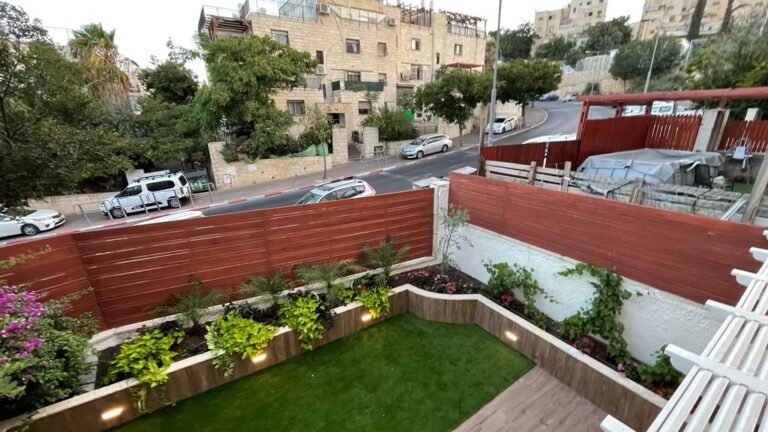 גדר עץ אופקית וגינה עם מדשאה ותאורה בחזית הבית