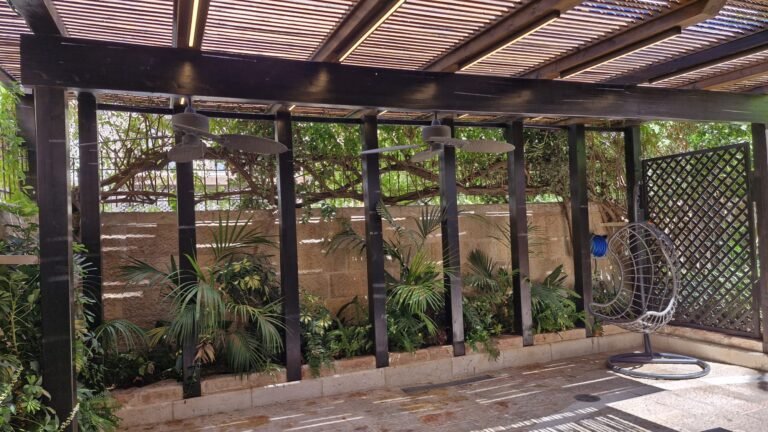 פרגולת עץ כהה עם קירות צמחייה ופינת ישיבה תלויה